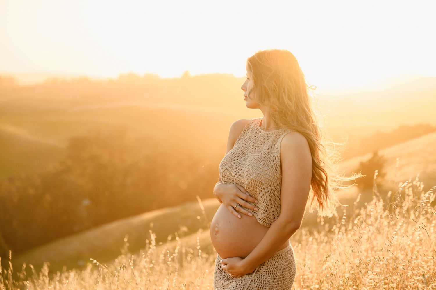 Pregnant woman posed in crochet two piece outfit in golden grass field in Newbury park holding her belly by Ventura maternity photographer