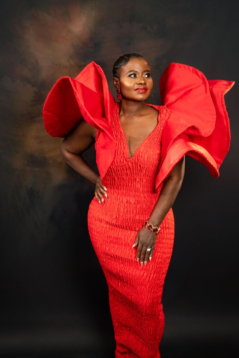 Fashion model wearing a vibrant red smocked dress with dramatic flutter sleeves strikes a dynamic pose against dark background.