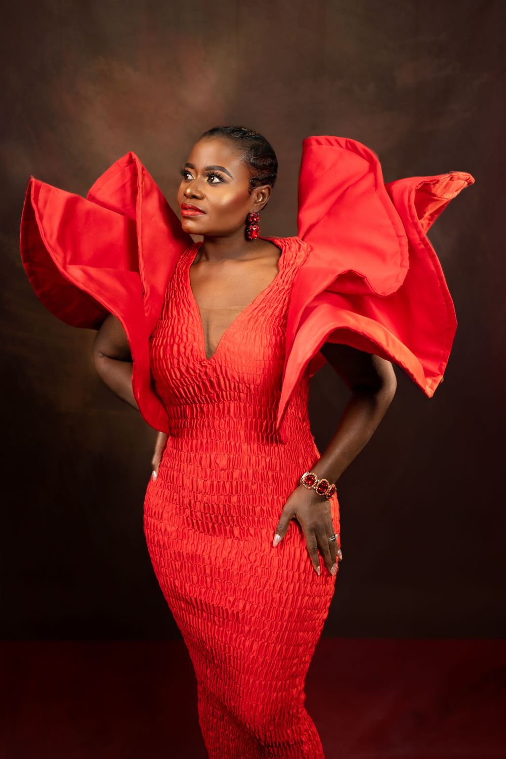 Elegant model poses in a fitted red dress with statement sleeves against moody studio backdrop.