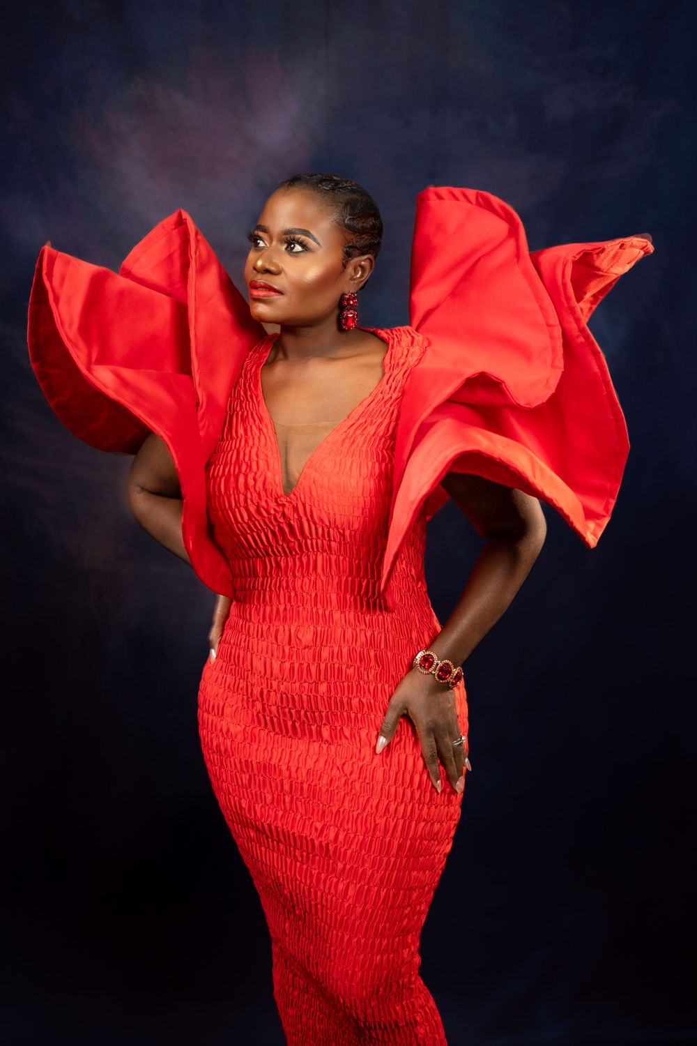 Textured red gown with dramatic wing-like sleeves photographed in artistic studio lighting.