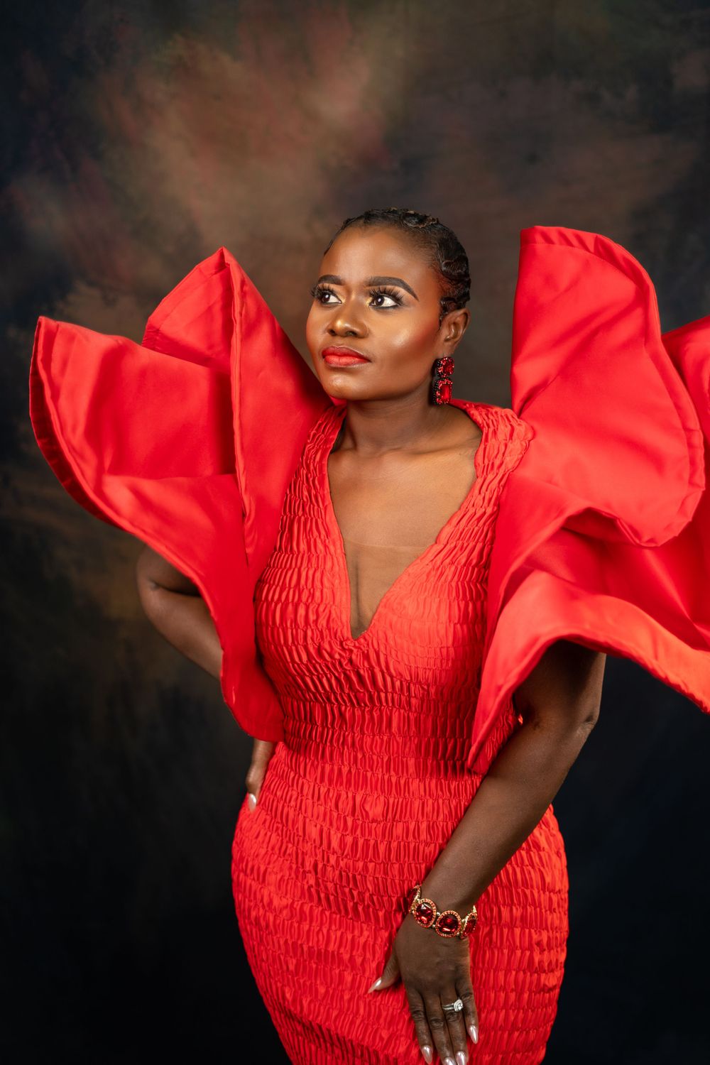 Fashion portrait featuring structured red dress with exaggerated shoulders in dramatic lighting.