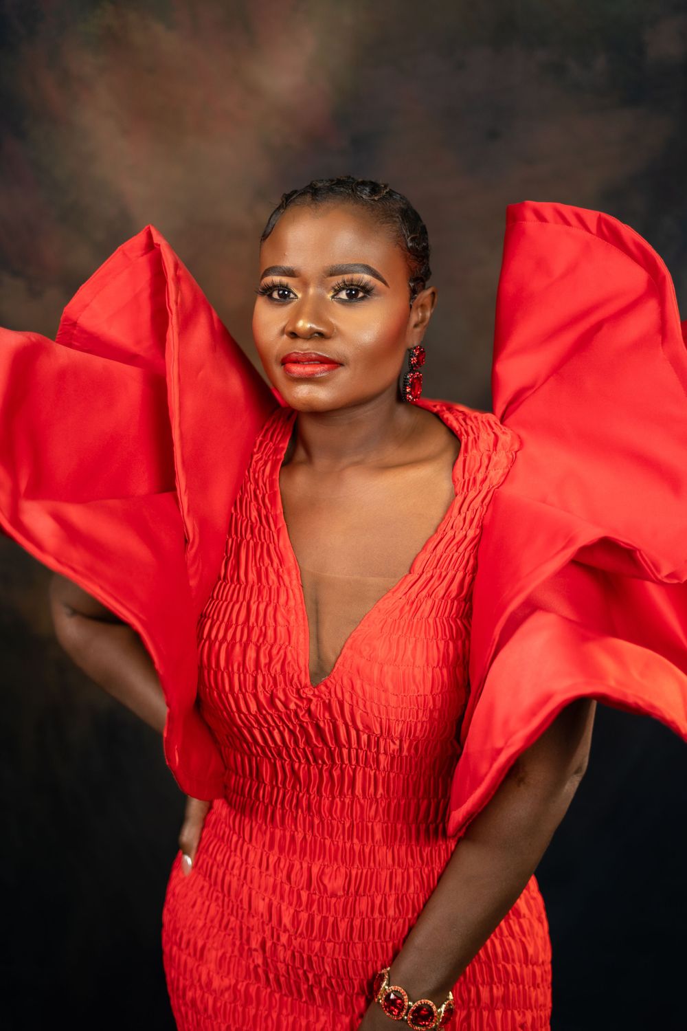 Model showcases striking red designer dress with sculptural sleeves in studio photoshoot.