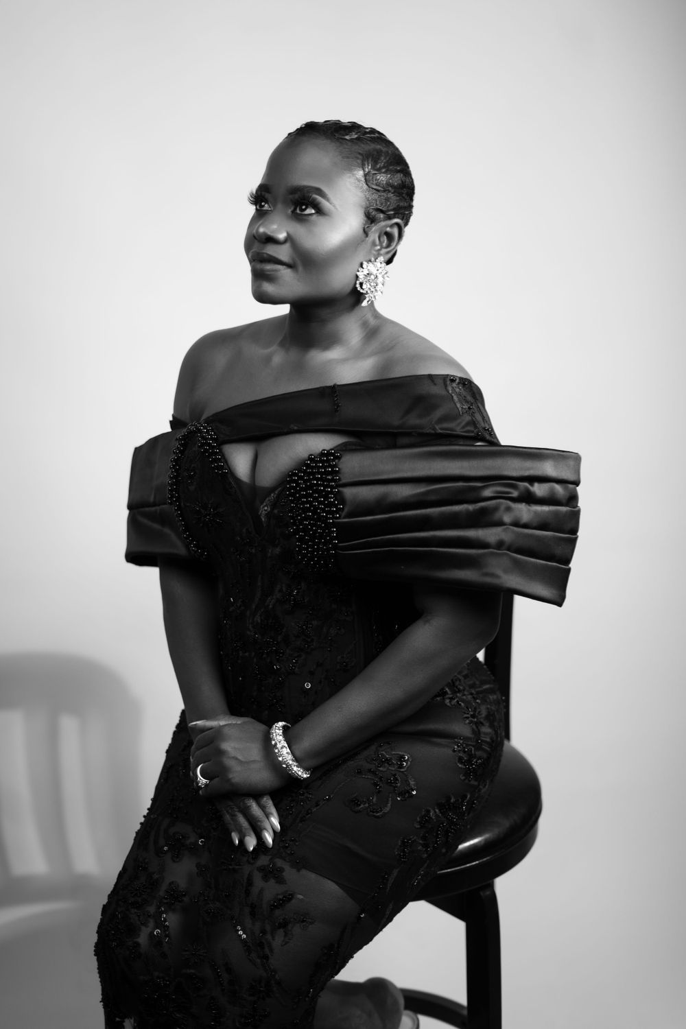 Black and white portrait showing model in elegant off-shoulder evening gown with textured details.