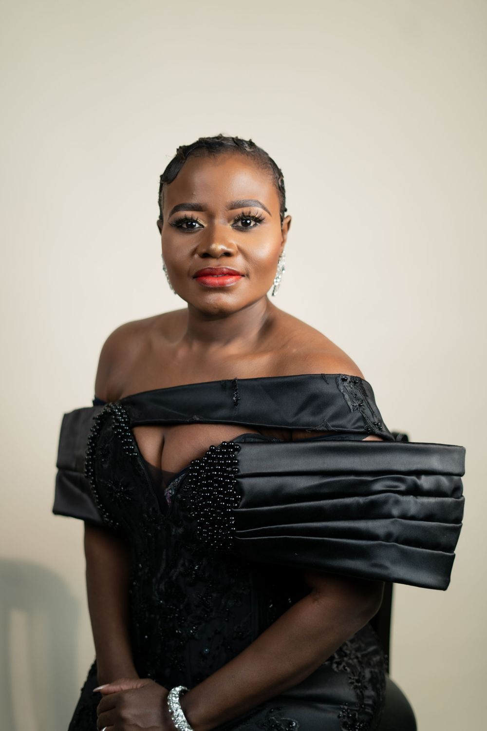 Studio fashion portrait in black formal dress with structured off-shoulder neckline and beaded embellishments.
