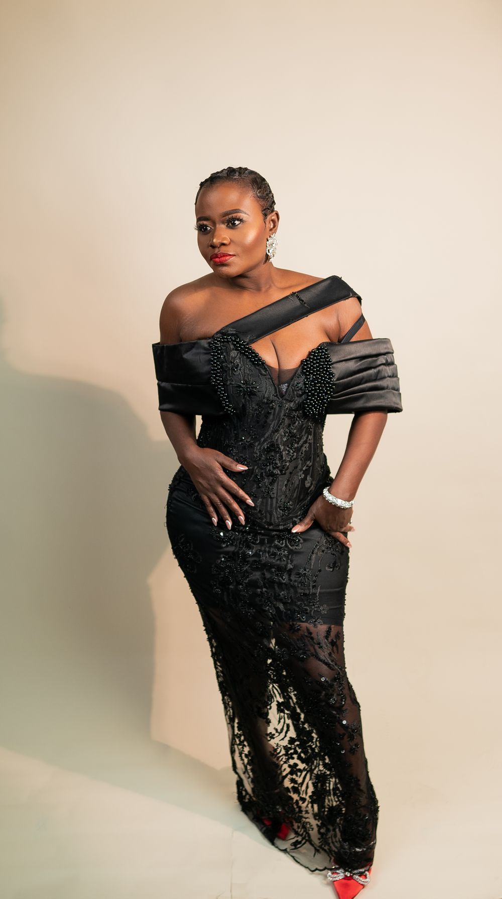 Full-length view of model in sequined black gown with structured bodice and red shoes.