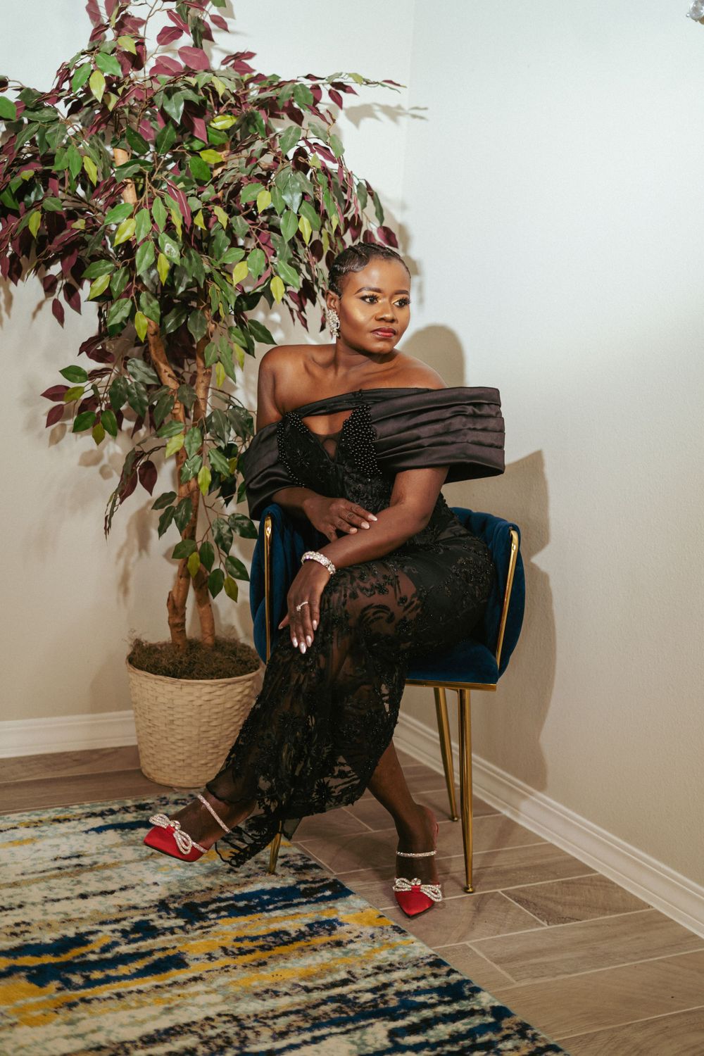 Elegant pose in off-shoulder evening gown beside potted plant.