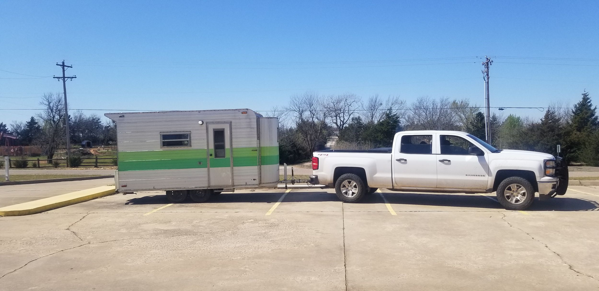 White pickup truck towing a retro mint green and white camper trailer on a concrete driveway.