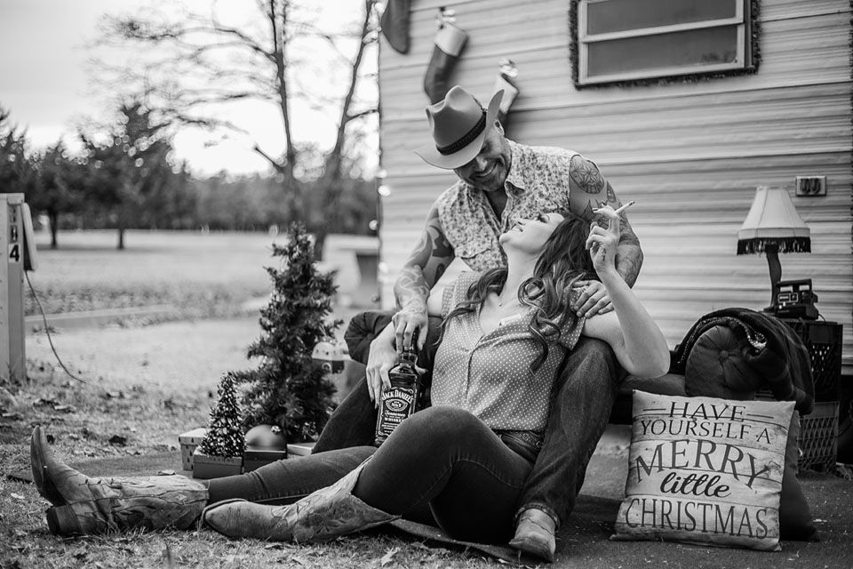 Black and white photo of holiday scene with decorated Christmas tree and pillows by vintage camper.