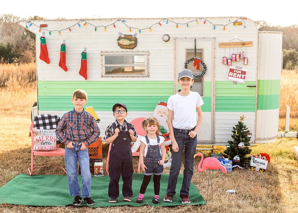 Family portrait in casual wear standing outside vintage camper decorated for Christmas.