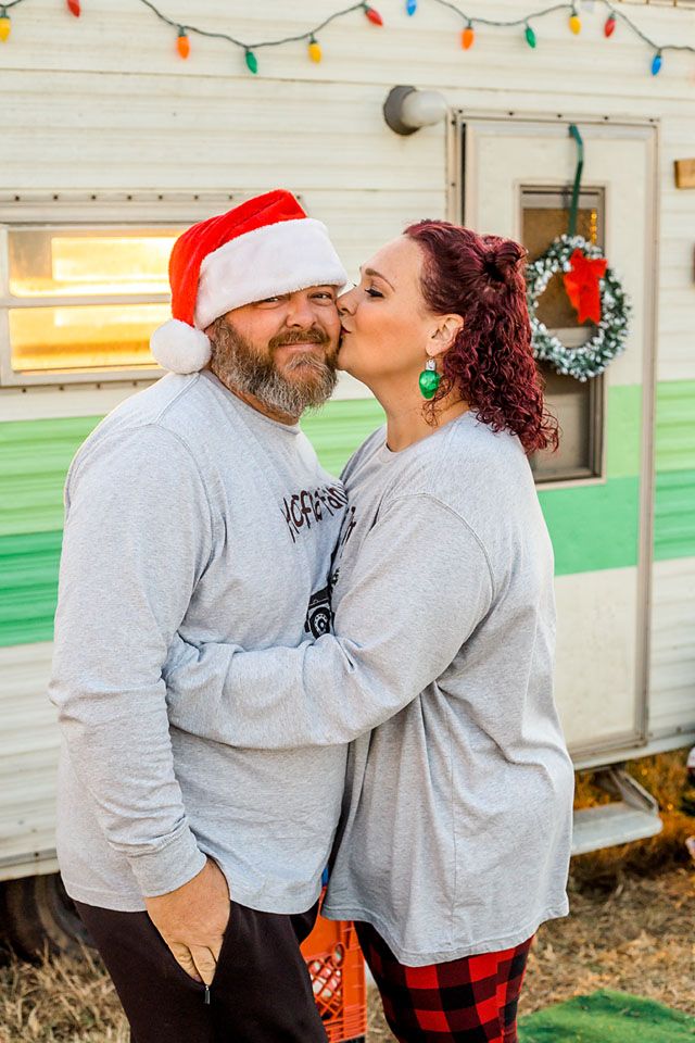 Couple in matching gray sweatshirts sharing a romantic moment by decorated vintage camper.