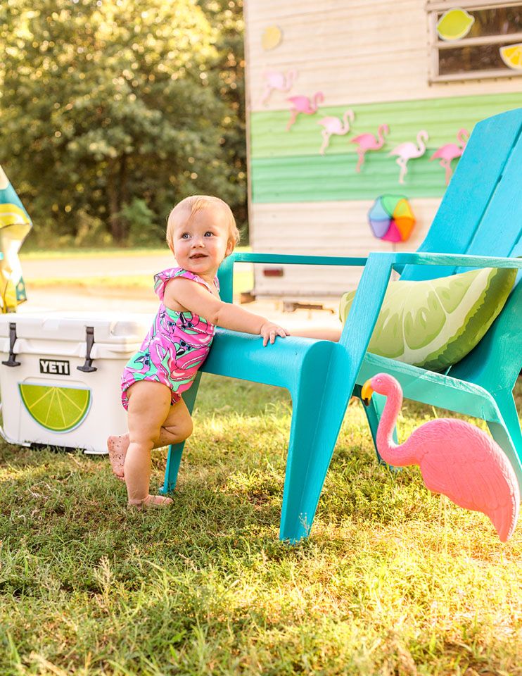 Colorful summer scene with turquoise chair, pink flamingo decor, and cooler by vintage camper.