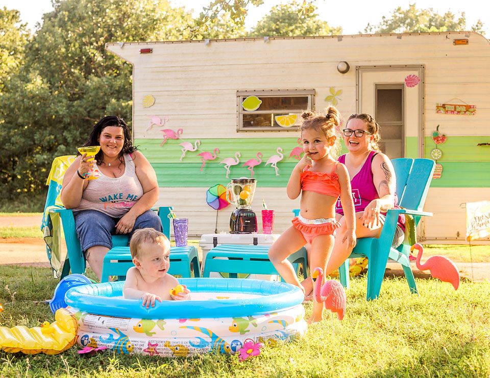 Group enjoying summer fun around an inflatable pool next to a vintage camper with festive decorations.
