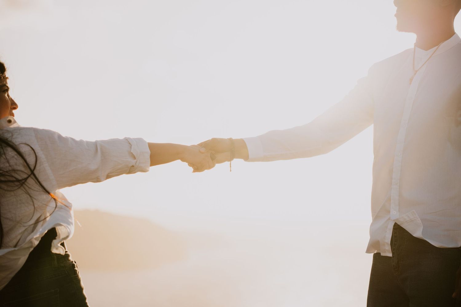 Two people holding hands in silhouette against bright sunset sky.