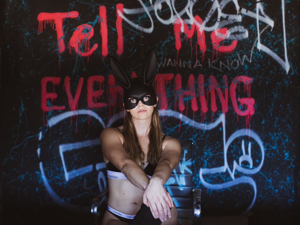 Urban photography against graffiti wall with 'Tell me everything' text in red spray paint.