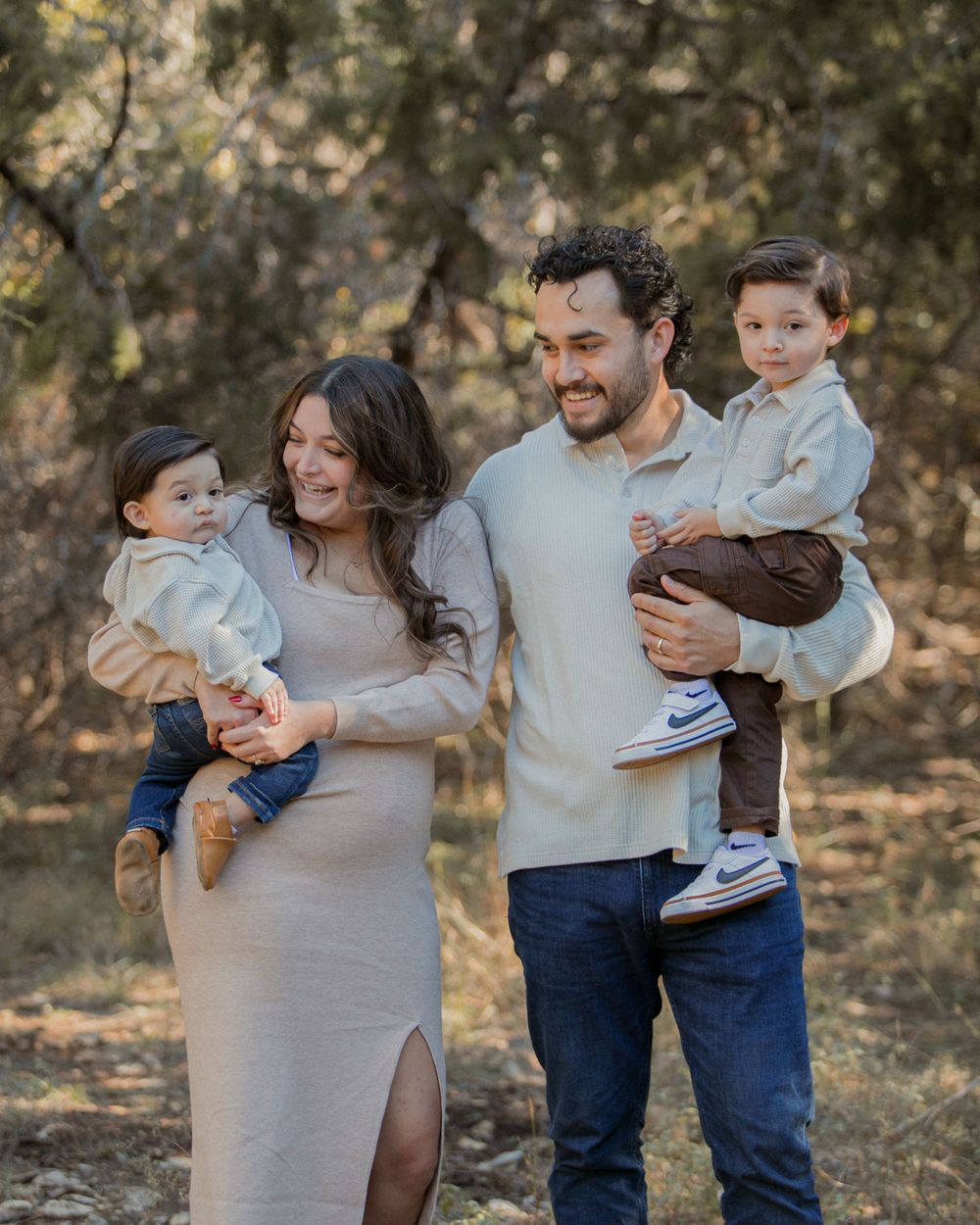 Family shares joyful embraces and laughter in a natural outdoor setting wearing neutral colors.