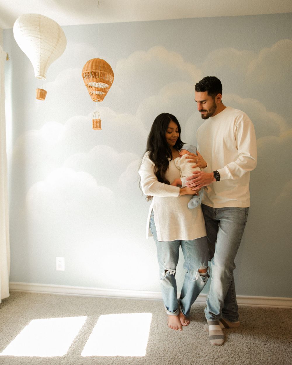 Couple shares playful moments in a sunlit room with white balloons against a gray wall.