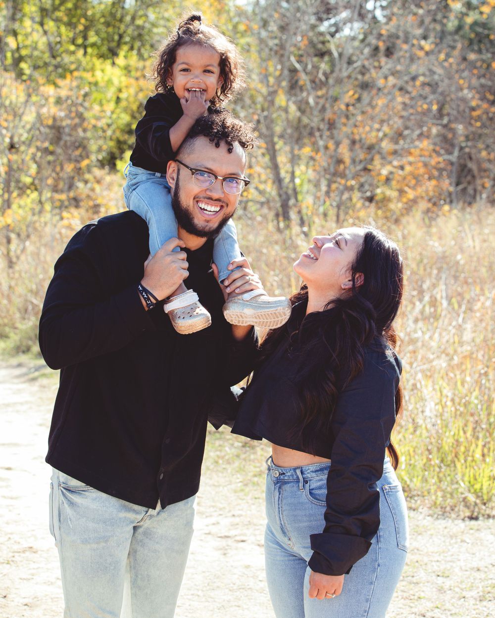 Couple shares playful moments and laughter in a sunny outdoor field with autumn foliage.