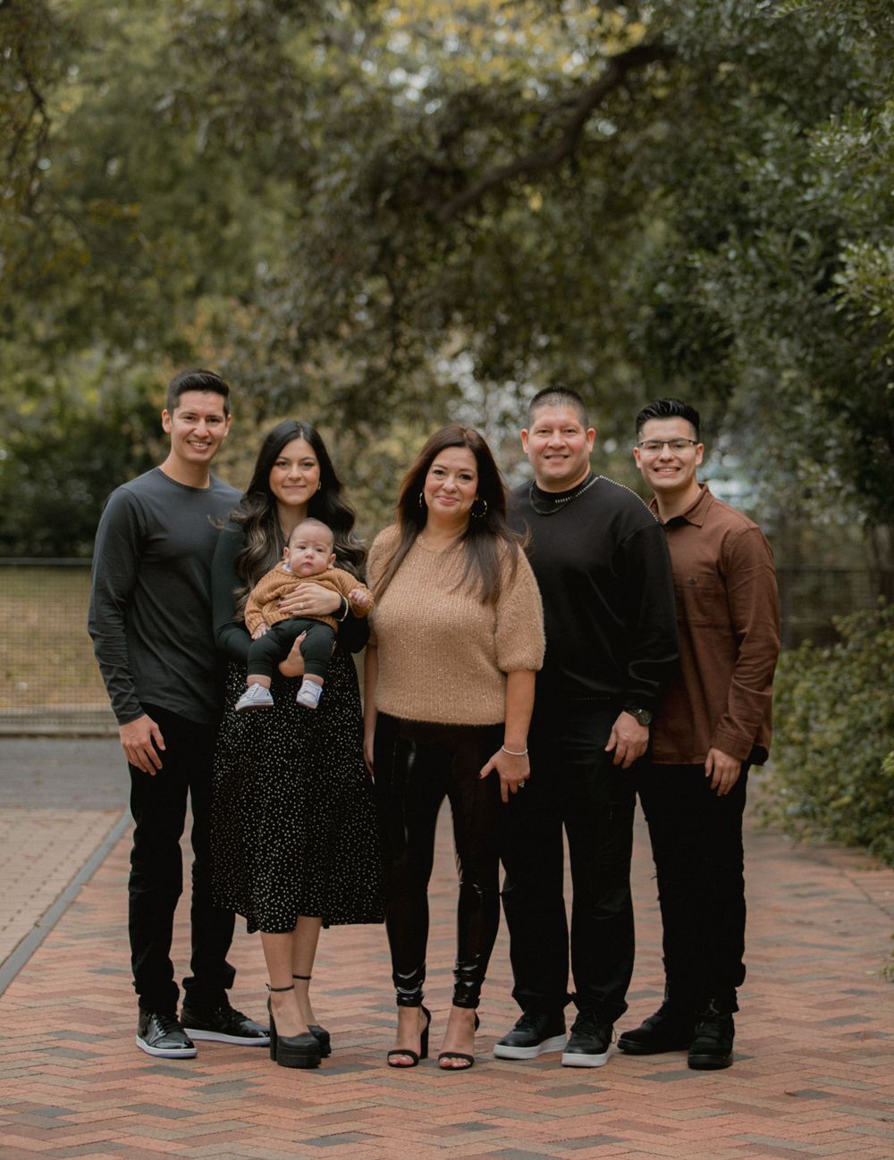 Family group poses together on brick pavement wearing coordinated dark and brown tones.