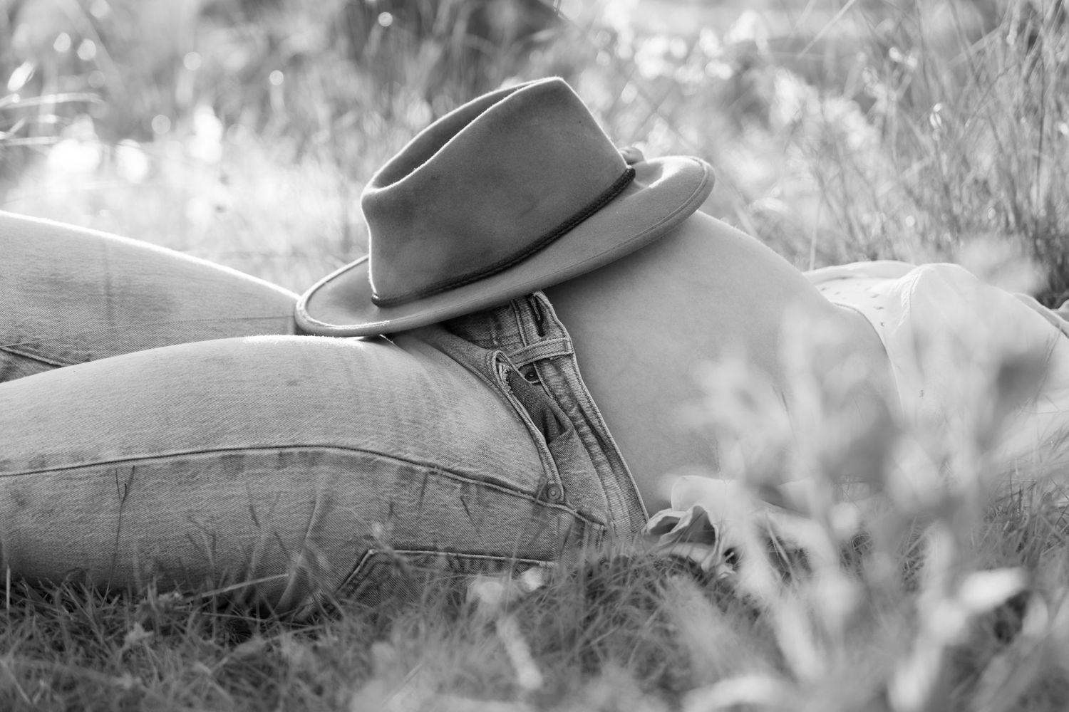A brown fedora hat sits against soft denim fabric in dreamy black and white photography.