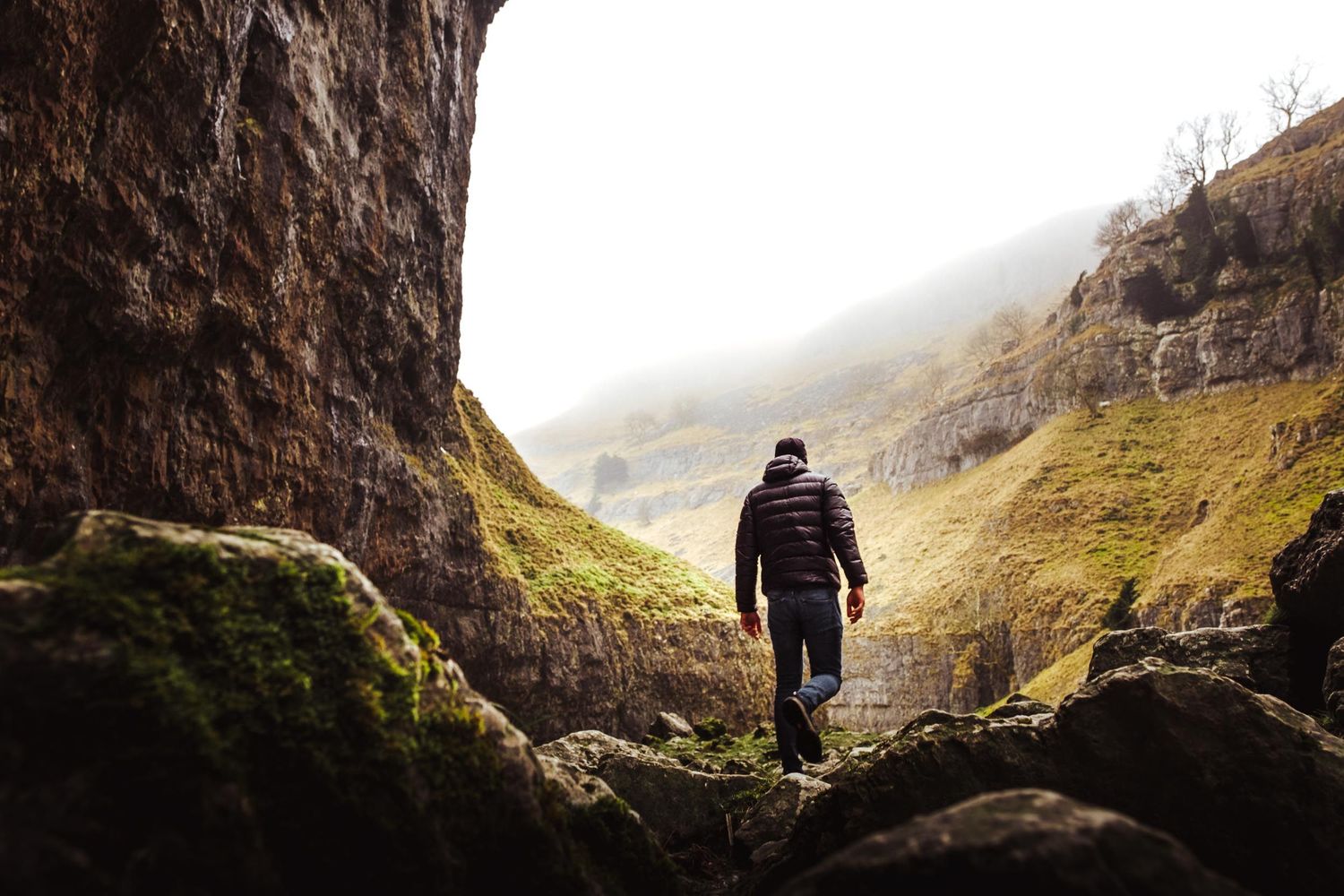 A silhouetted figure walks through a misty mountain landscape with dramatic cliffs and atmospheric lighting.