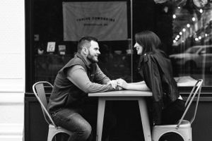 A couple sits at a small table having an intimate conversation at a cafe in black and white.