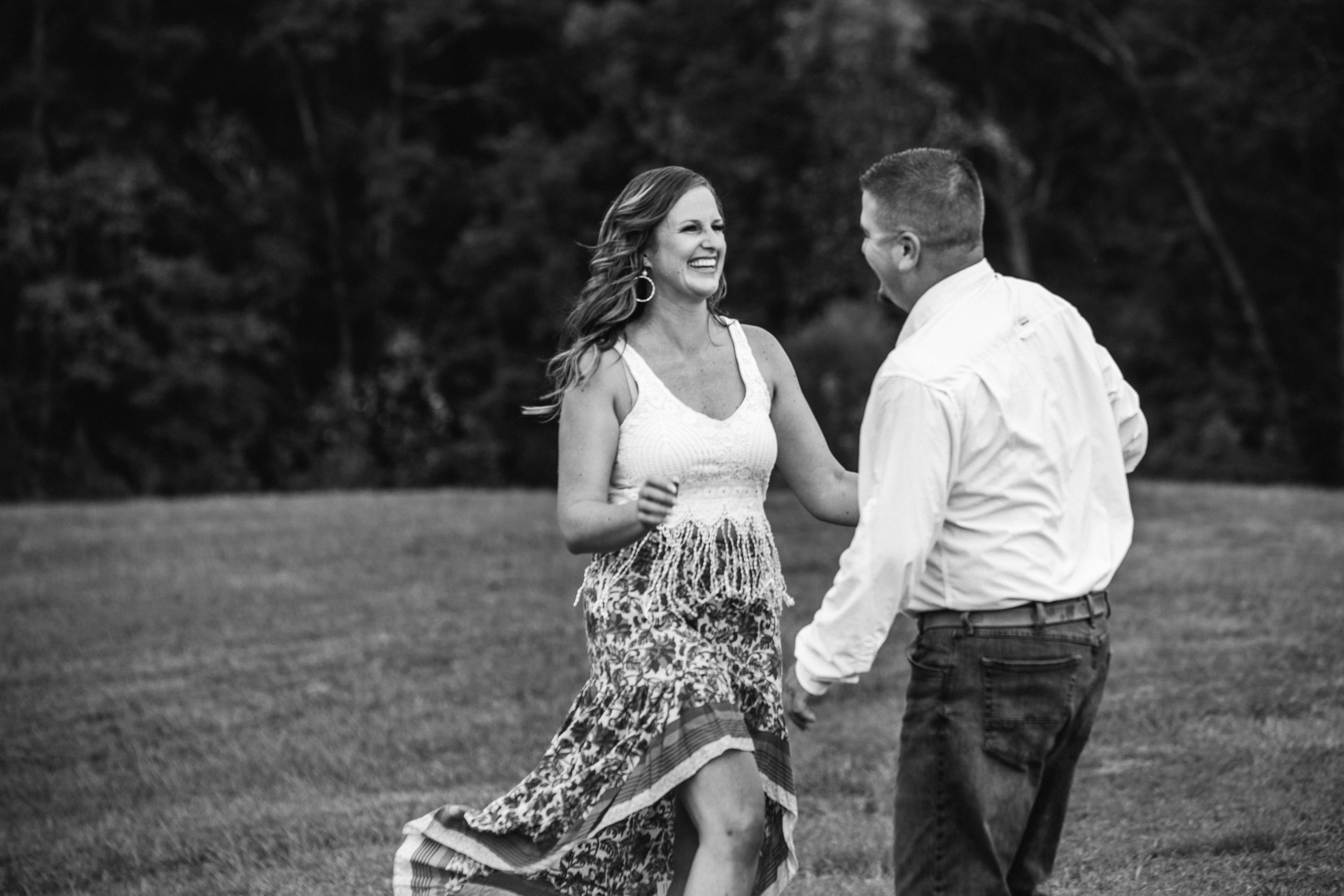 A happy couple dances together in a grassy field on a summer day, captured in black and white.