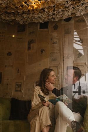 Person in a cream knit sweater sitting by a window in a cozy room with decorative paper-covered walls and ceiling.