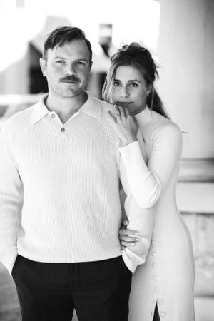 A black and white portrait of a couple posing together, with the woman in a light dress and the man in a sweater.