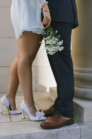 A romantic wedding photo showing white bridal heels and brown groom shoes on stone steps with delicate baby's breath flowers.