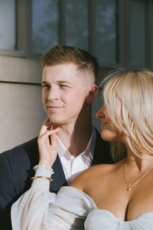 A romantic couple shares an intimate moment outdoors, with the woman affectionately touching the man's chin.