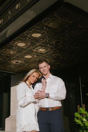 A couple stands intimately beneath an ornate ceiling with decorative metalwork and recessed lighting.