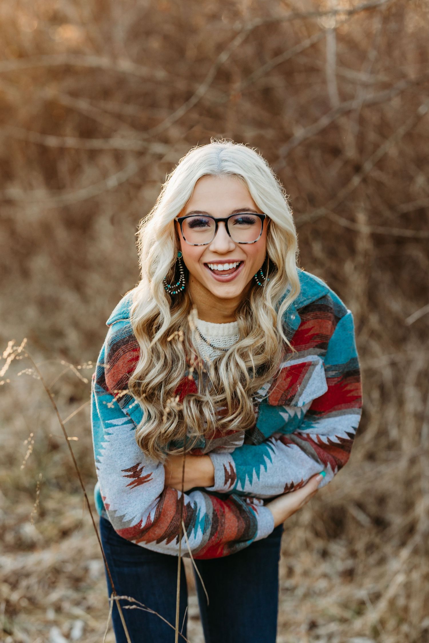 Woman in colorful patterned sweater smiles outdoors during golden hour.