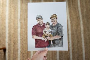 Hand holding a watercolor portrait painting of two men and a baby, family artwork gift illustration.