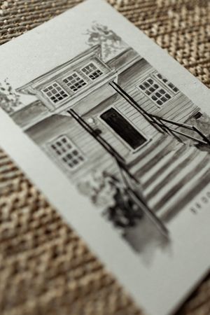 Angled view of a detailed pencil sketch of a two-story house with stairs and railings on white card.