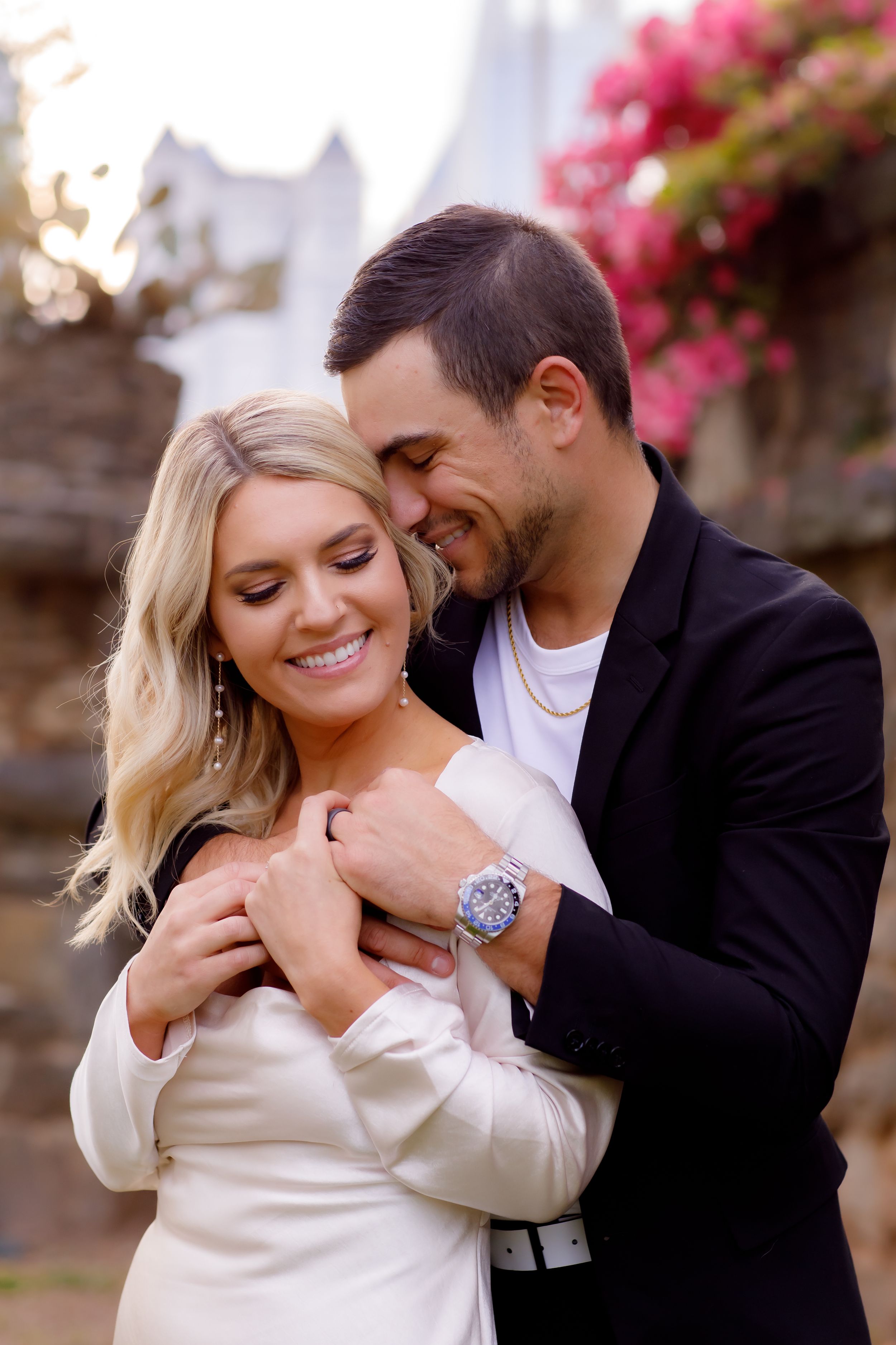 Intimate engaged couple moment captured with pink bougainvillea flowers in background.