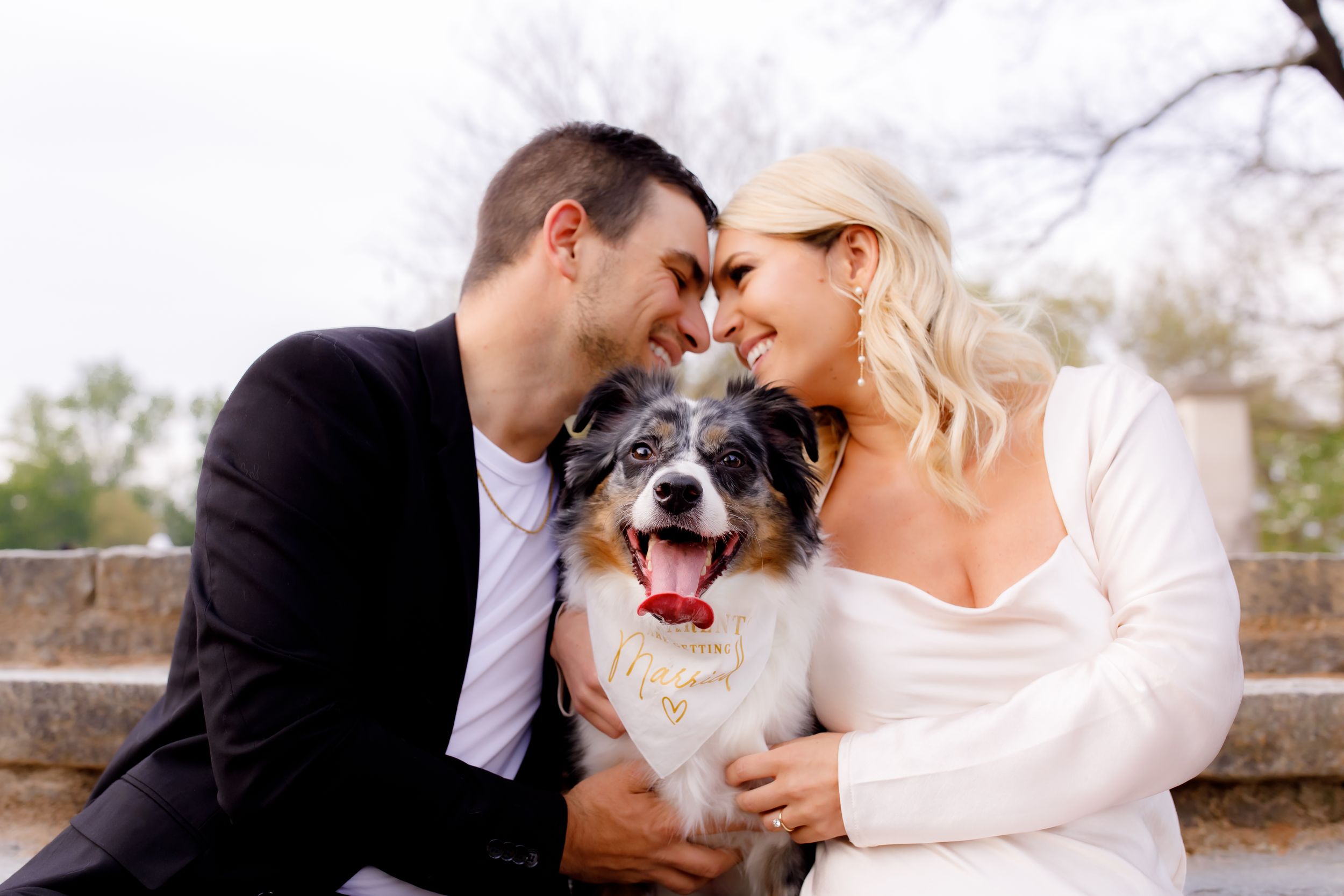 Happy couple shares tender moment with their smiling dog during wedding photoshoot.