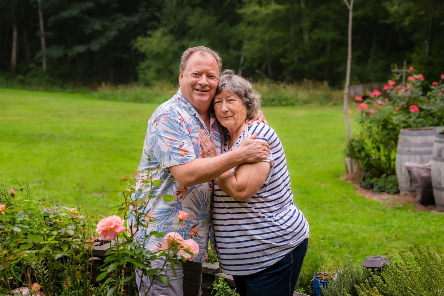Smiling sibling couple embracing in a lush garden with roses and green trees in the background.