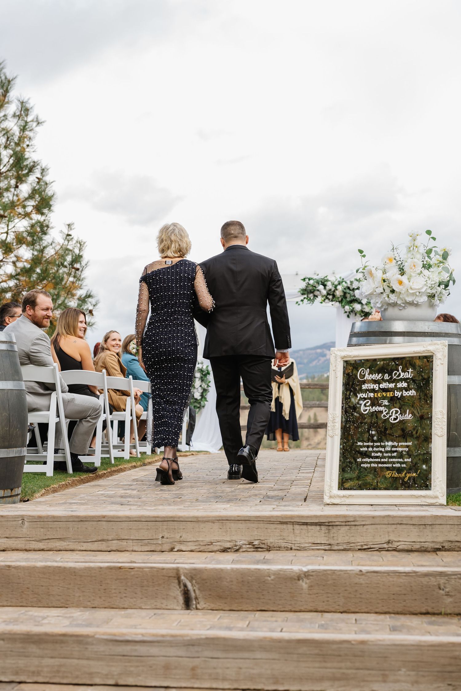 Wedding guests sit on rustic wooden benches overlooking a scenic mountain landscape during an outdoor ceremony.