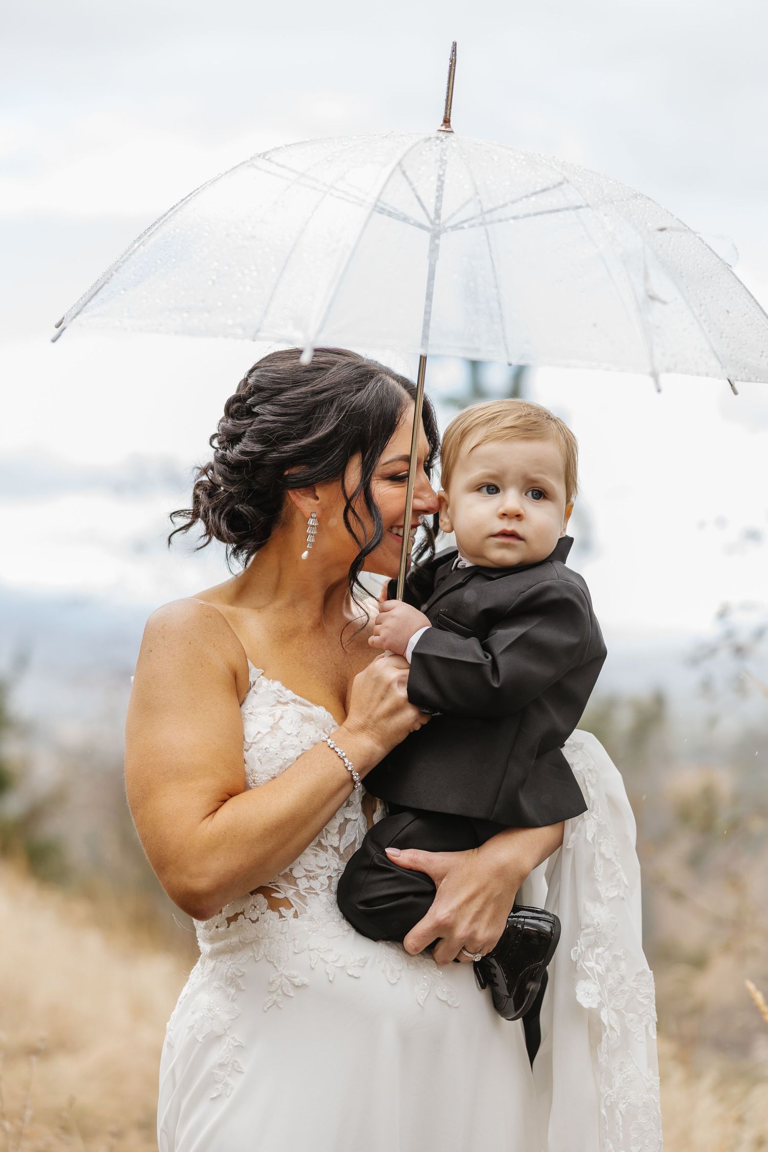 A tender moment captured between a bride in a white dress and a small child under white umbrellas.