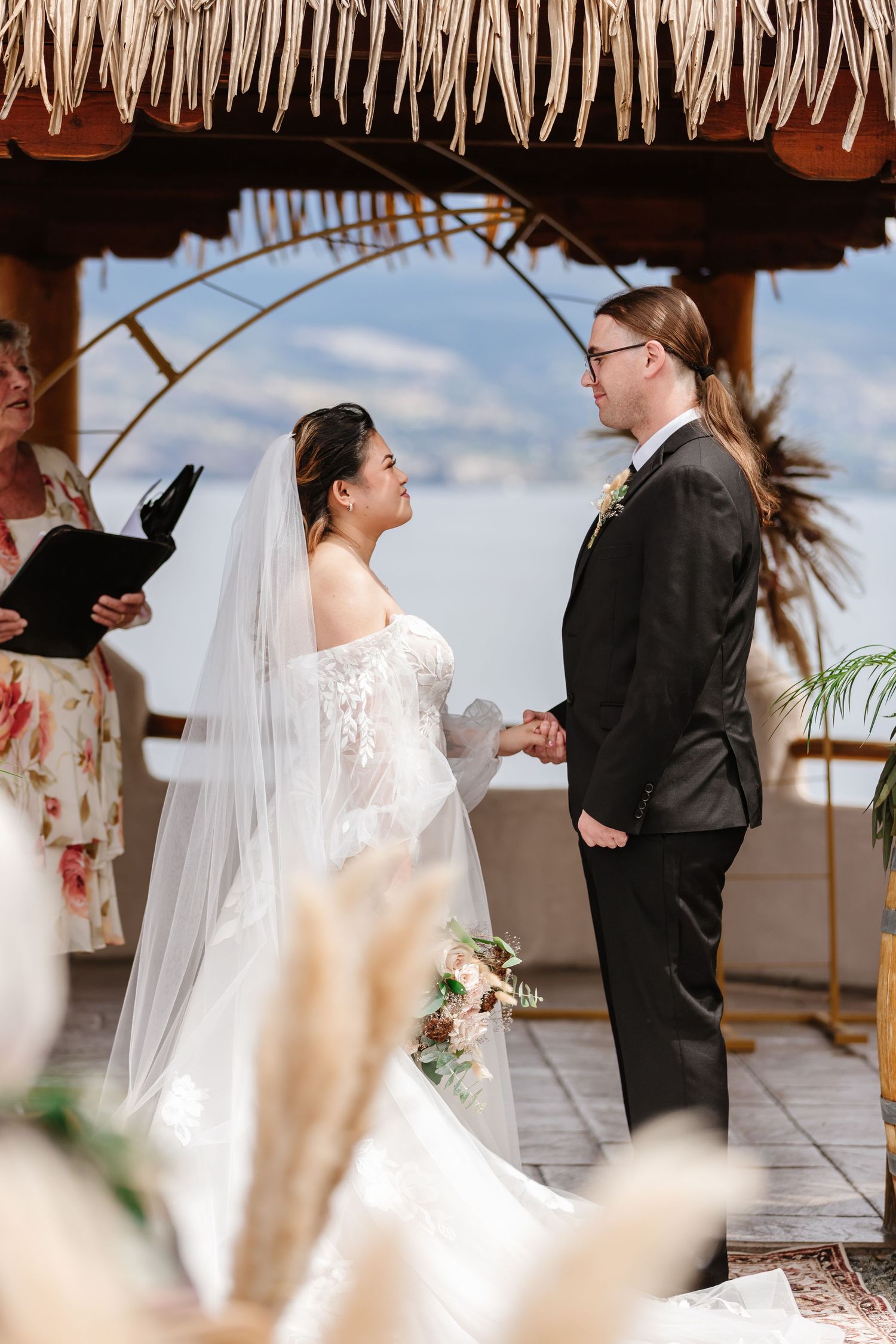 Couple exchanges vows under a palm-thatched canopy during their tropical wedding ceremony.