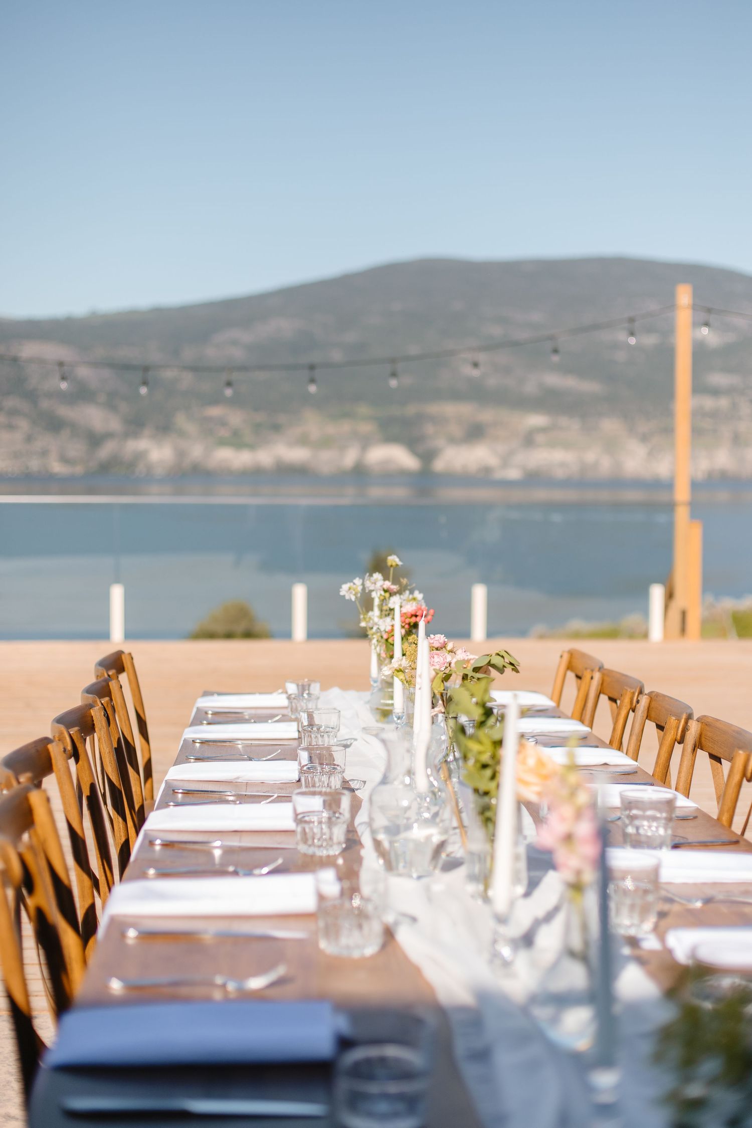 Elegant outdoor wedding reception table setting overlooking a scenic lake and mountain landscape.