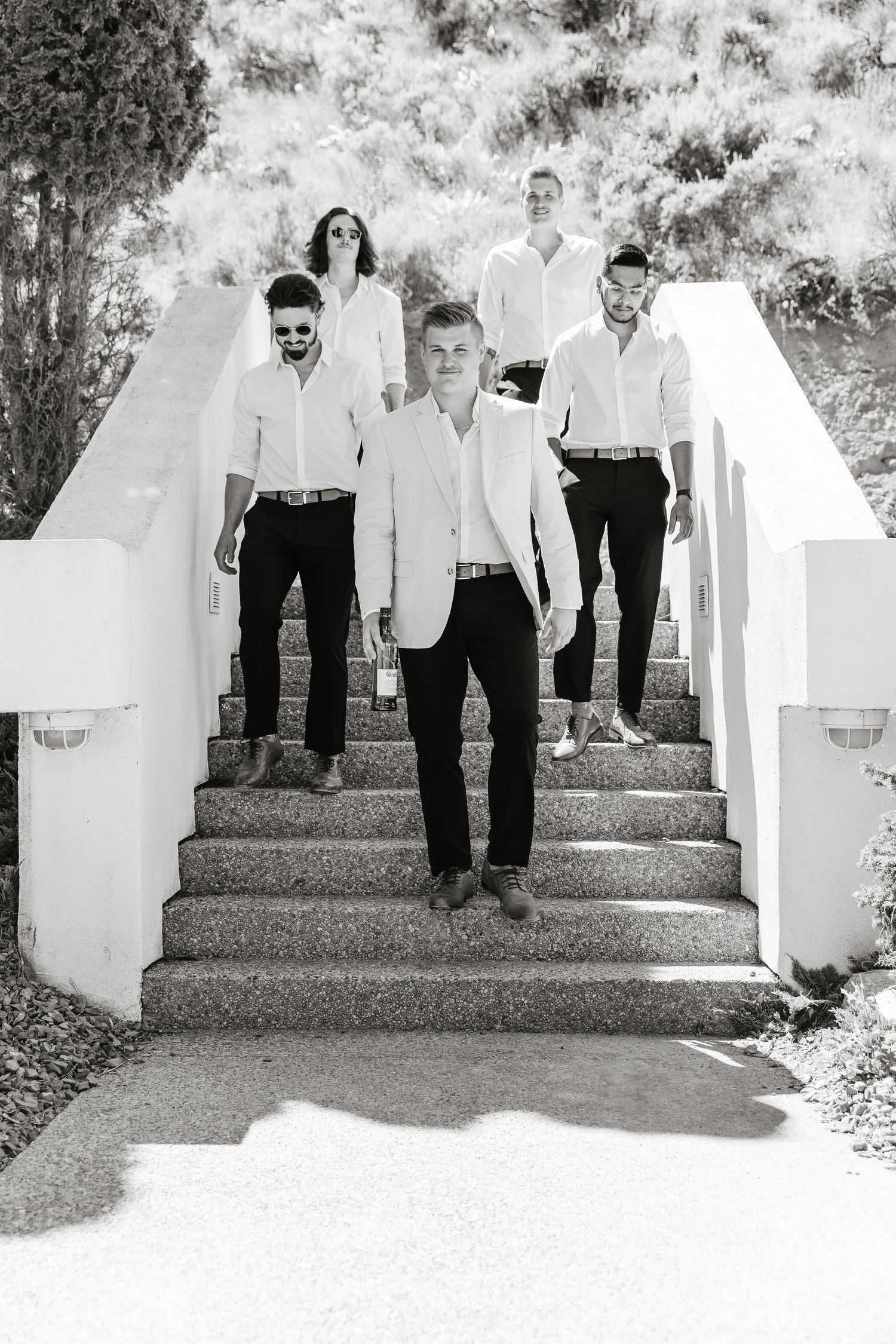 A black and white photograph shows a group of people standing on white outdoor steps in formal attire.