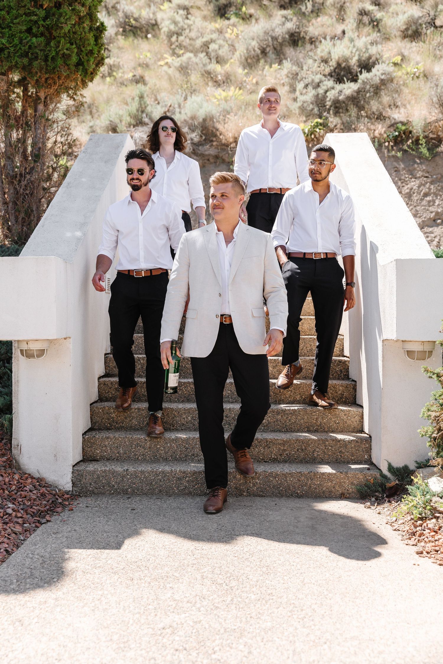 Wedding party in white shirts and blazers posing on white stone steps outdoors.