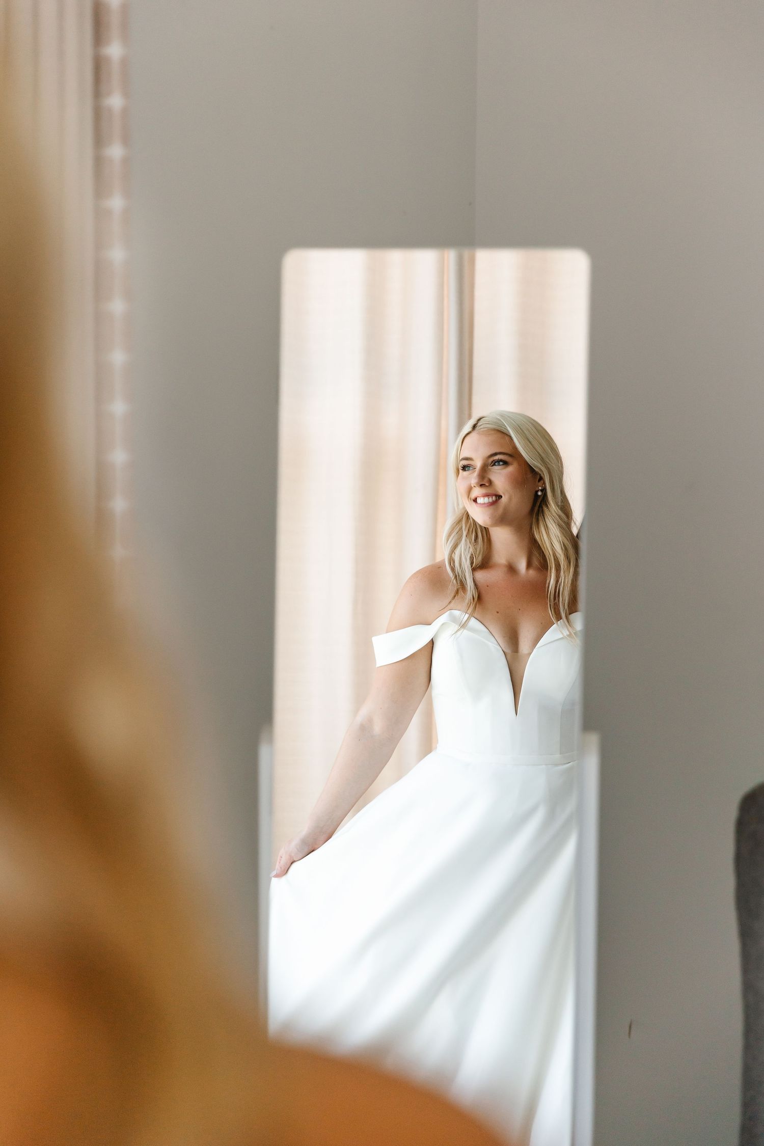 Artistic fashion portrait with warm tones showing figure in white dress near sunlit window.