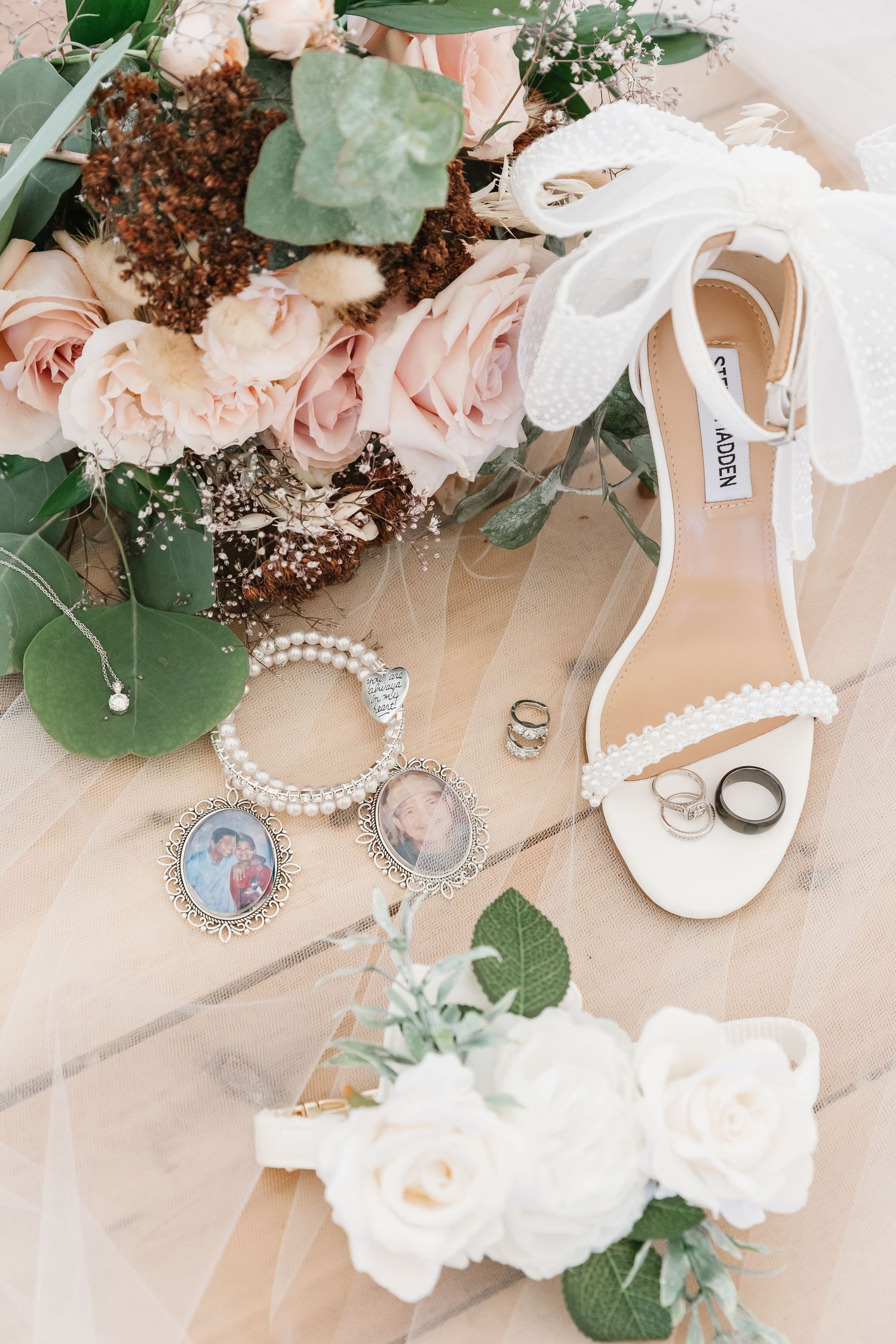 Wedding accessories including white sandals, pearl jewelry, and delicate floral arrangements on a light beige background.