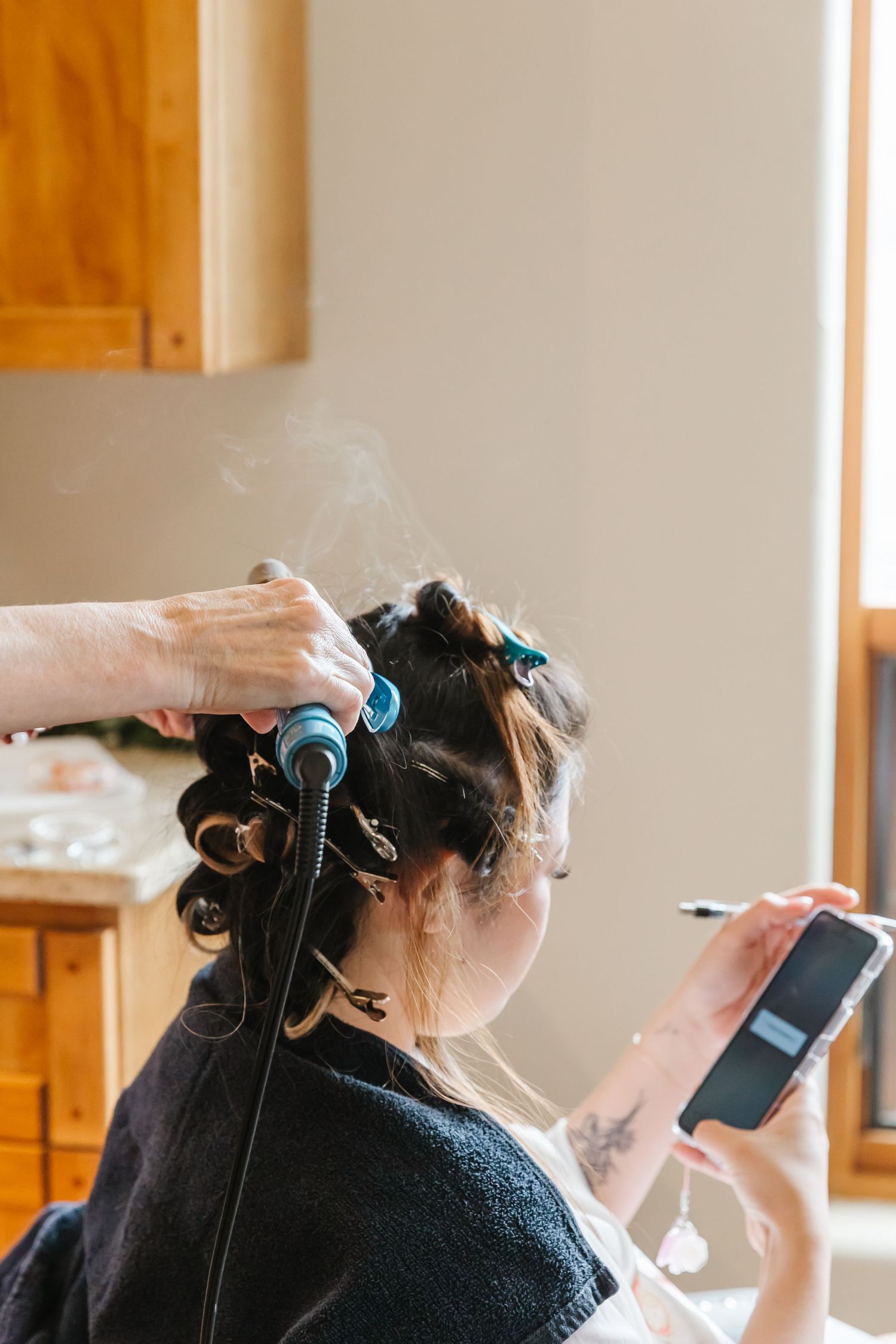 A person getting ready for a wedding with hair curlers and styling tools in a sunlit room.