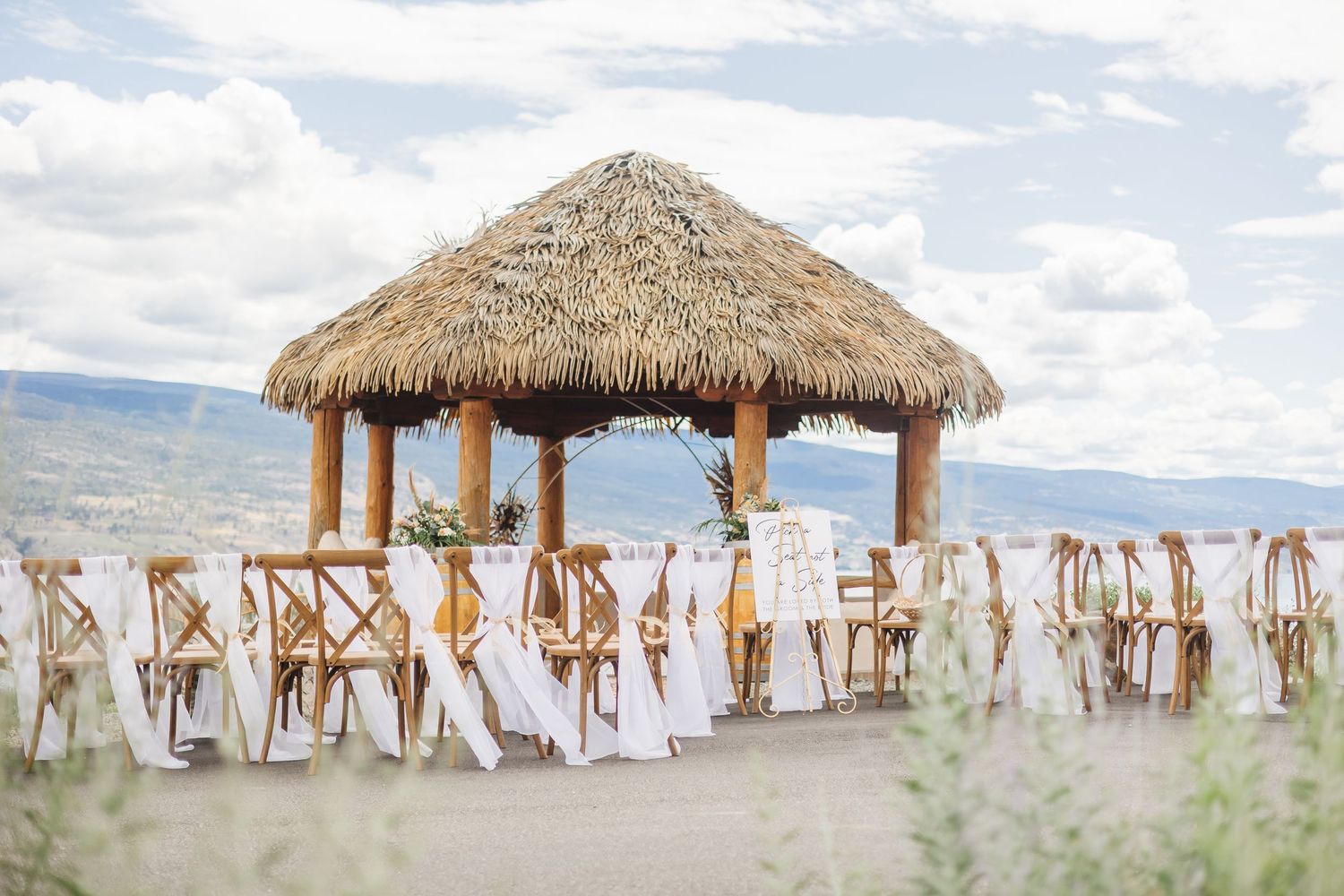 A beachfront wedding ceremony setup with thatched-roof gazebos and white fabric decorations along the coastline.
