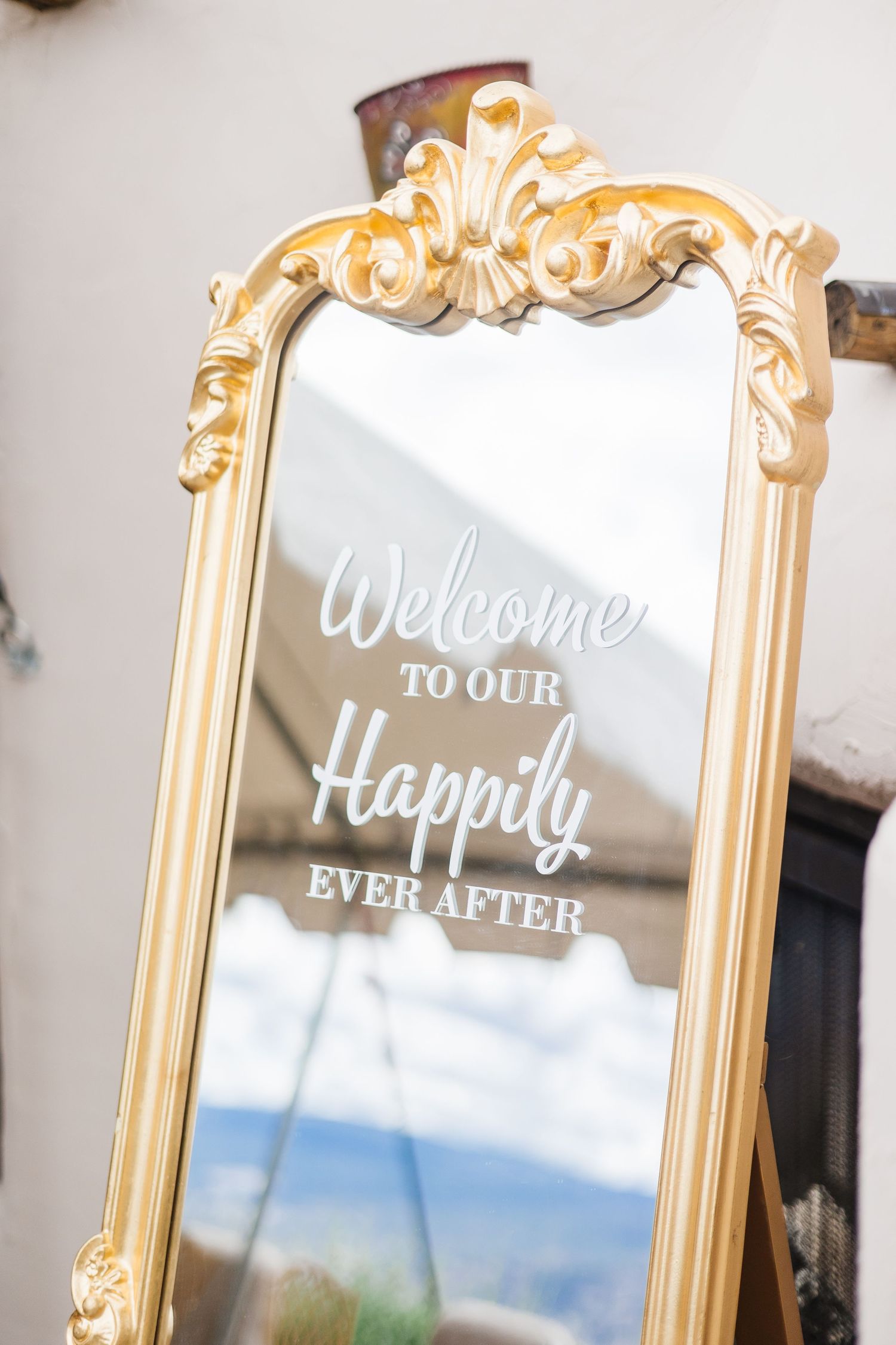 Elegant gold-framed mirror with white calligraphy wedding signage displayed against a light wall.