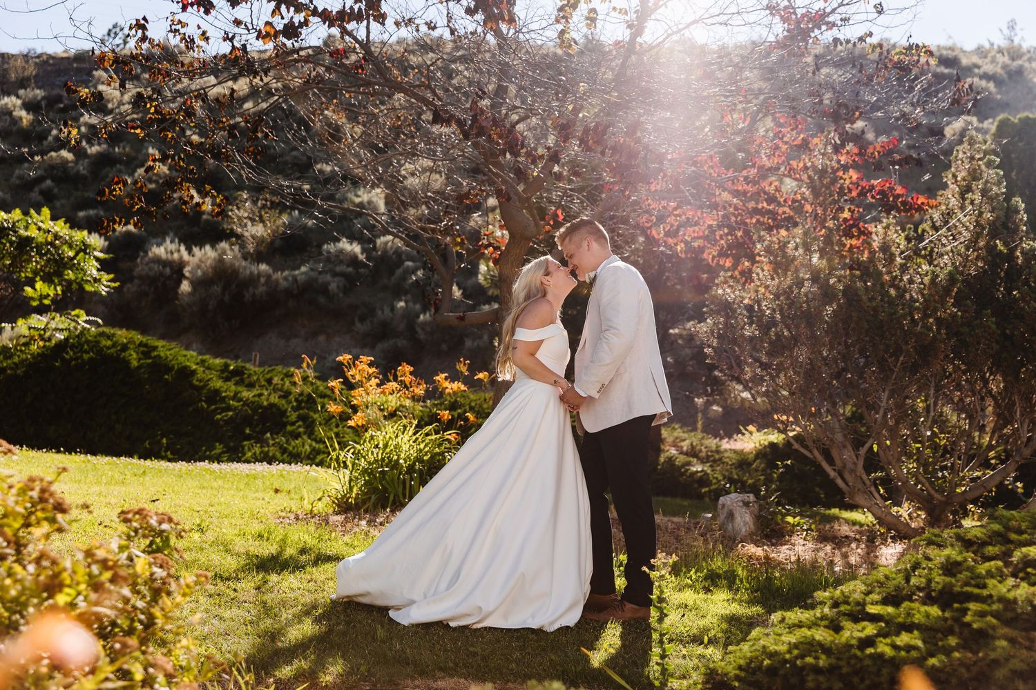 A couple embraces in a sunlit garden with autumn foliage and colorful flowers on a beautiful afternoon.