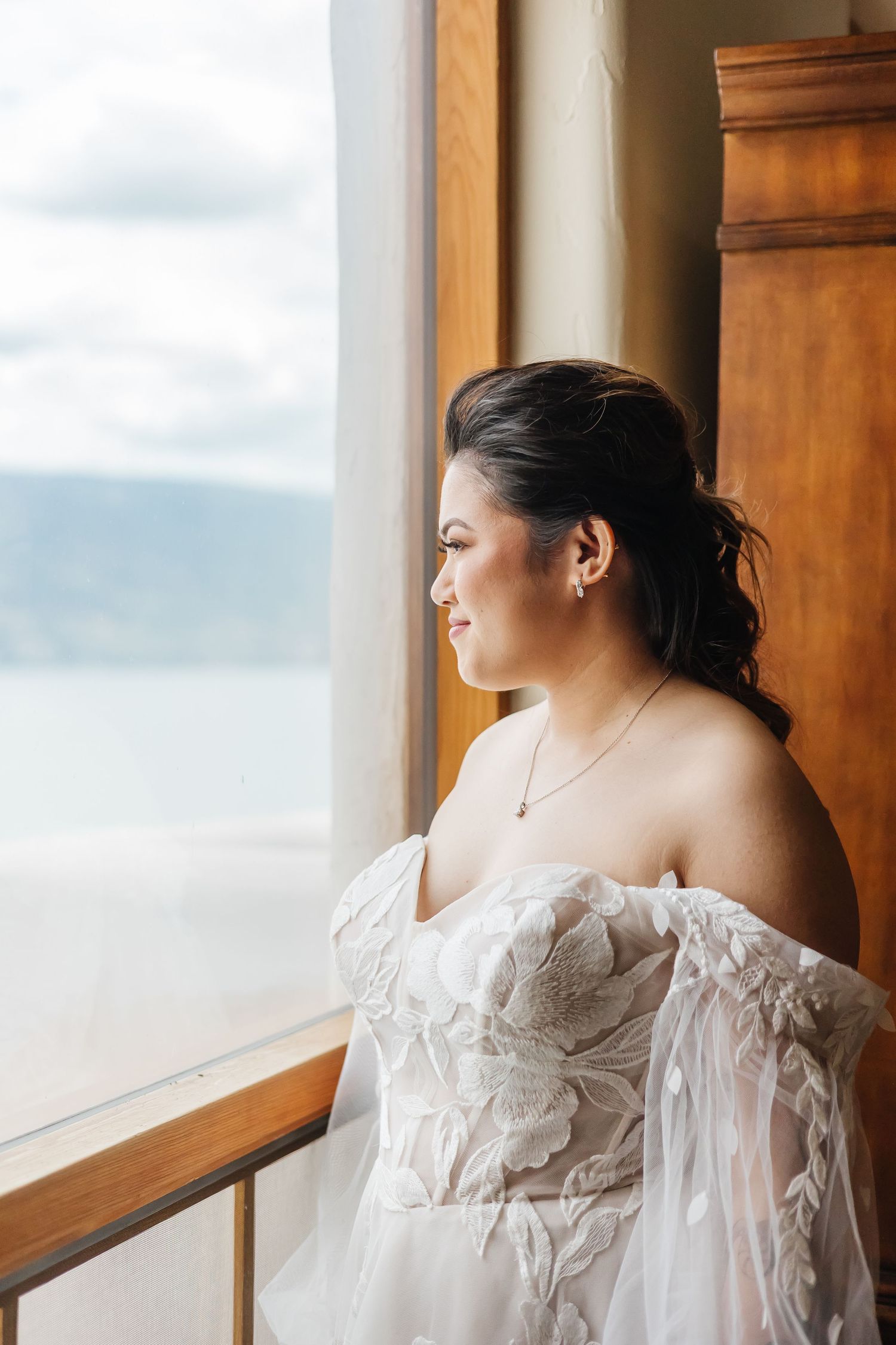 An elegant white wedding dress with delicate lace and sheer details framed by a window with scenic views.